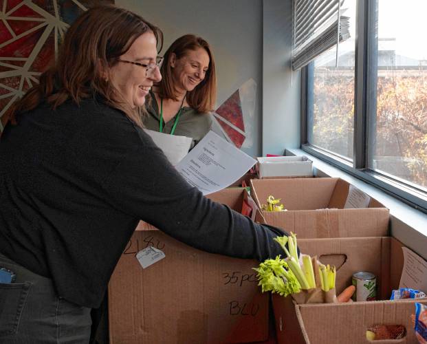 Sarah Bate, an intern, and Lisa Gallant, a clinician with the Bridge Family Resource Center, add recipes and directions to boxes filled with fresh food items, turkeys, and craft activities for 45 families for the Thanksgiving Day holiday.