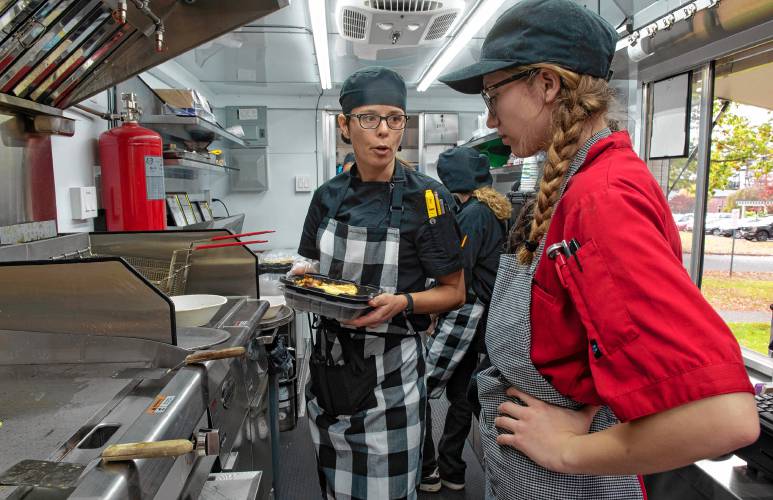 Brenda Fortin, one of the chefs at Smith Vocational and Agricultural High School, helps junior Jorjia Young  cook one of the items on the menu on opening day of the culinary  program’s new food truck. The truck will be open in front of the school Friday morning and for Friday night’s fall festival.  